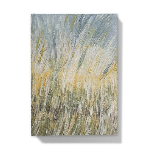 Wheat fields Hardback Journal has an abstract image of wheat swaying in the fields of golds light sage greens & light blues towards the sky.