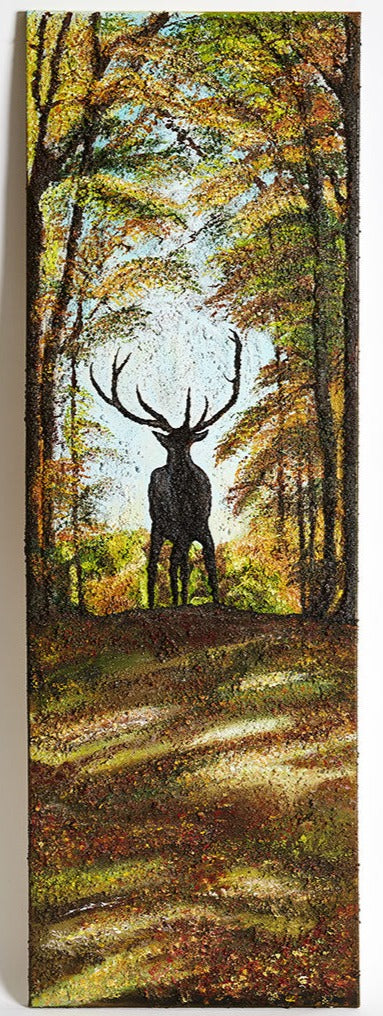 Wall Art Canvas Print Proud Stag.  A proud stag standing in the center of of path in a forest at the cusp of the path, with large antlers. He is shadowed by tall trees either side of him and the light from behind. Blue sky above the autumnal leaved forest. Light coming through the trees casts light on the path before him with colourful leaves that have fallen to the ground.