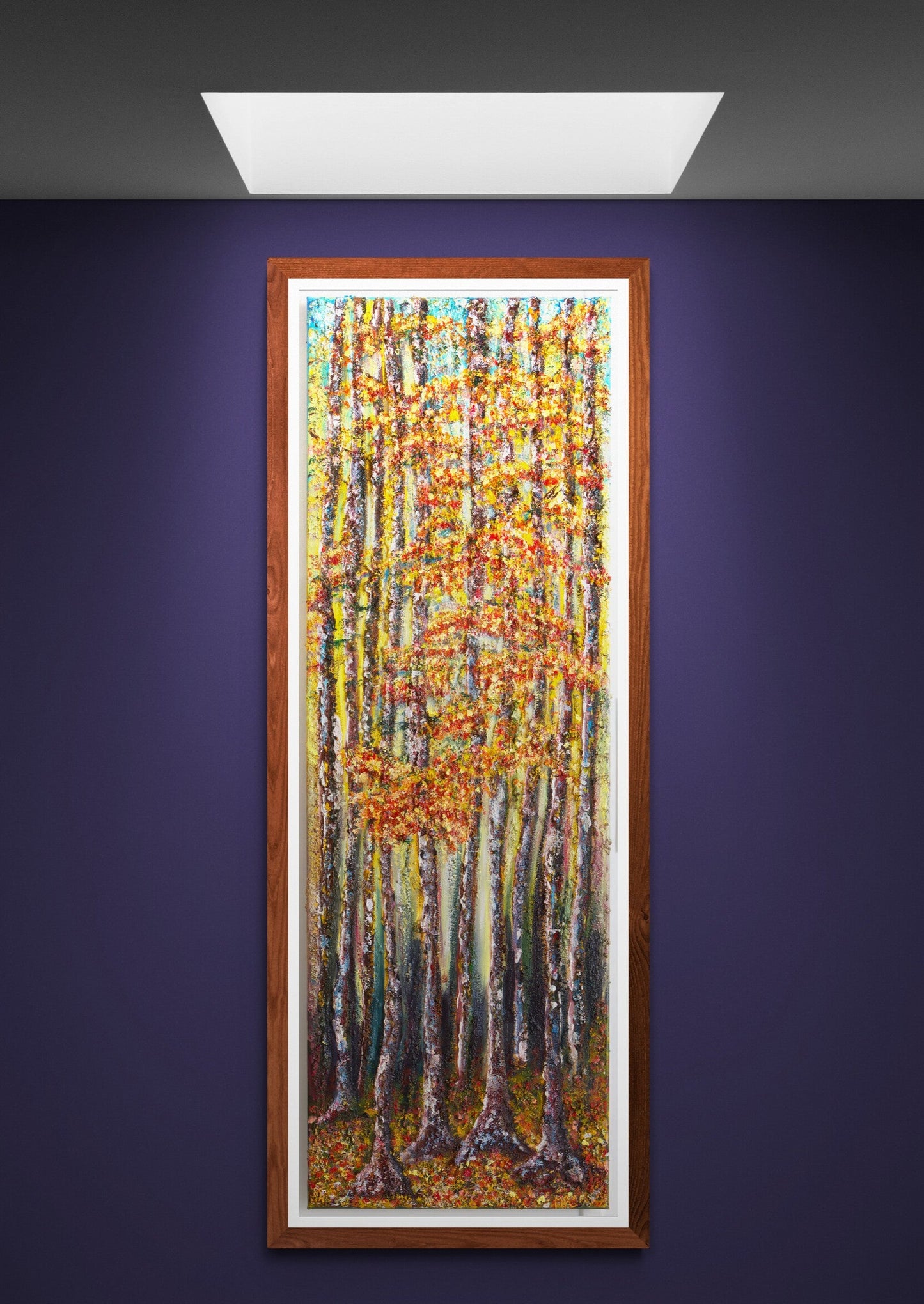 Wall Art canvas 120 x 40 cm of a forest scene deep within the forest. Very tall trees with strong trunks painted with hues of mauve's and blues in the light behind them also, leading to lighter shades as the light changes towards the sky, of pale blue & hints of clouds. The leave are a mix of autumnal colours, golds, reds and bronzes, as is the floor of the forest, where the floor is carpeted with fallen leaves of autumn