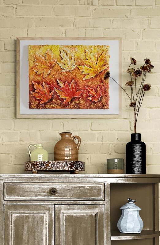 Wall Art Canvas Print painting of golden colours of autumn of maple leaves. Six leaves three above the other three which are golden in colour, underneath caramels & bronzes. The original piece has lots of texture as this piece has all the same looks & nuances without the lumps & bumps to feel. . Painting has been mounted & framed & hung on a beige coloured wall  Painting has been framed in a light coloured frame and mounted onto a oat coloured brick wall